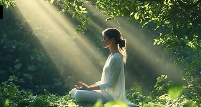 A woman meditating in a forest as soft rays of light fall through the leaves